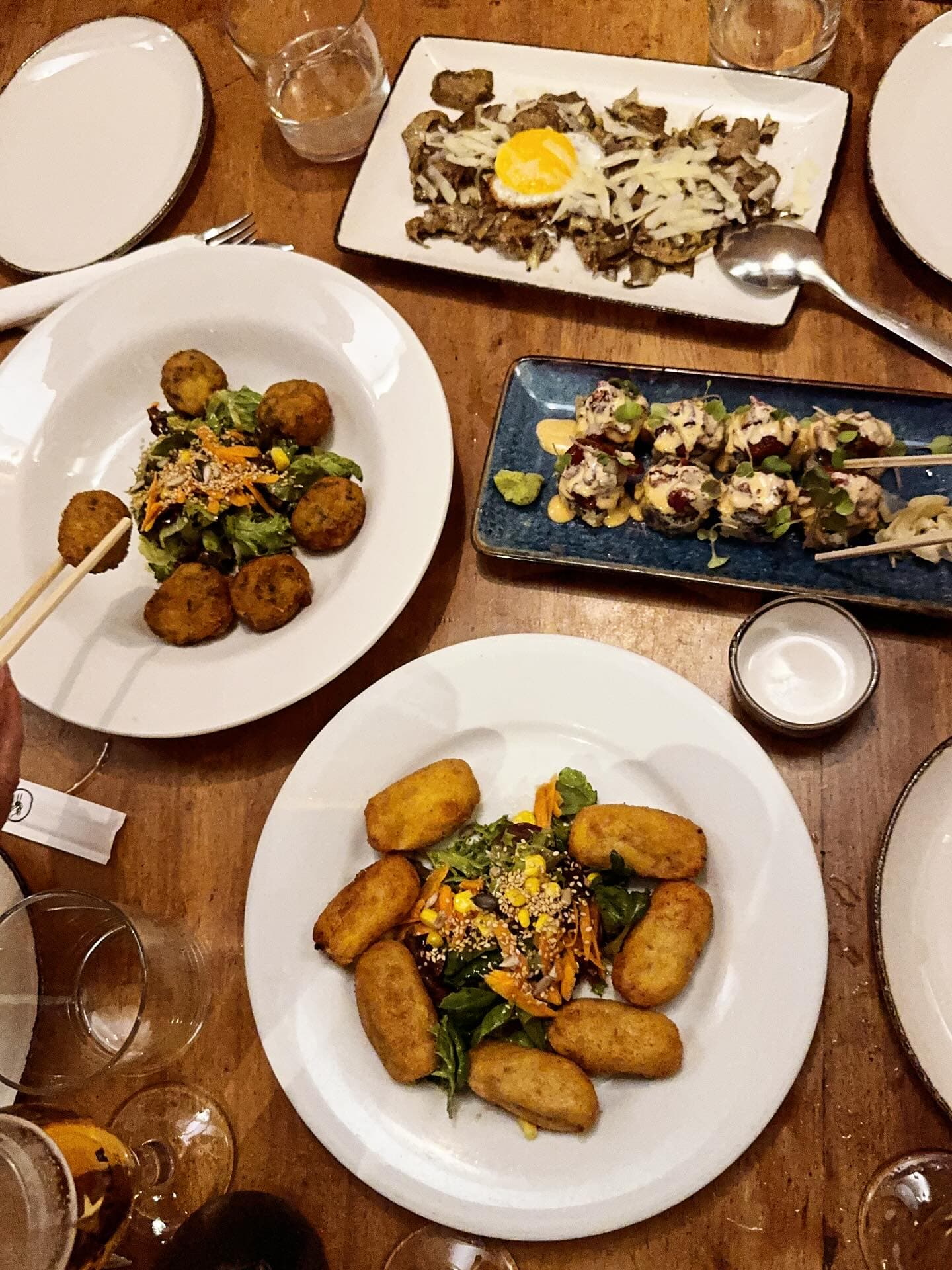 Mesa con croquetas, ensalada, rolls de sushi y un plato con huevo y queso